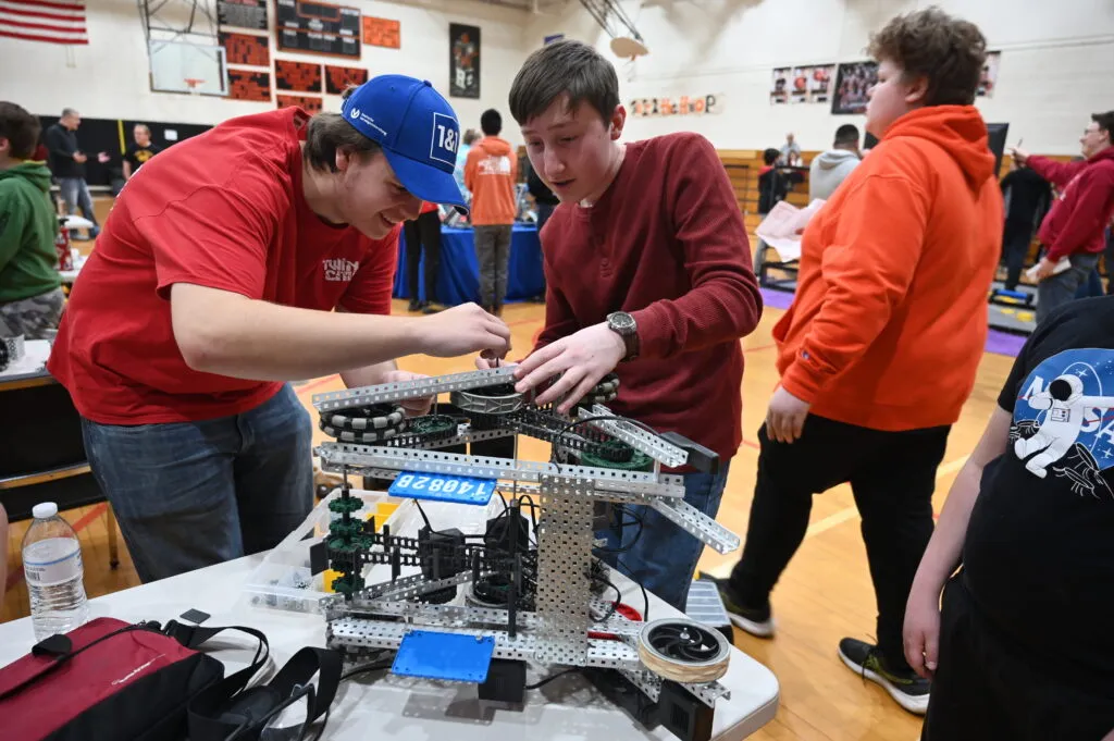 Two high school students in a gymnasium working on a competition robot for the robotics competition.